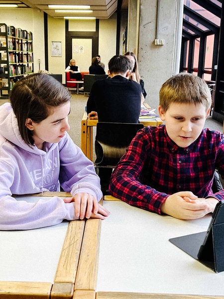 Eine Jugendliche Nachhilfelehrerin sitzt neben einem ihrer Schüler an einem Tisch der Bibliothek in Kerpen.