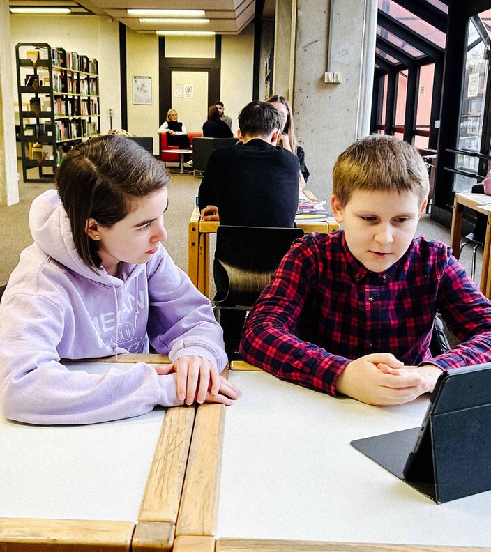 Eine Jugendliche Nachhilfelehrerin sitzt neben einem ihrer Schüler an einem Tisch der Bibliothek in Kerpen.