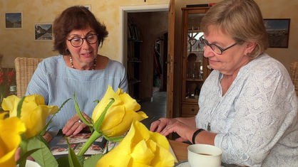 Karin Bonse und Hildegard van Lier sitzen am Wohnzimmertisch und sehen sich ein Fotoalbum an