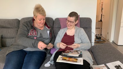 Britta Tenberge und ihre Schwester Kerstin sitzen zusammen auf einem grauen Sofa und betrachten alte Fotos.
