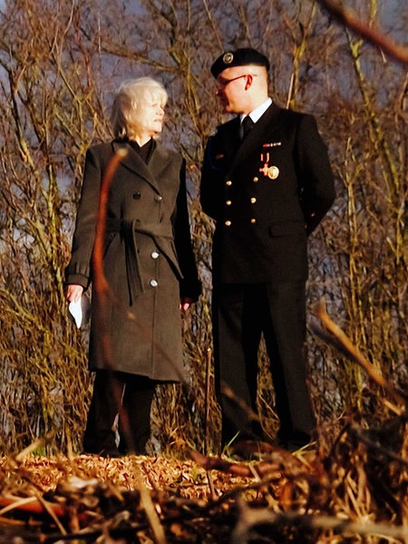 Ein Mann und eine Frau stehen nebeneinander an einem spätherbstlichen Wald und schauen sich an. 