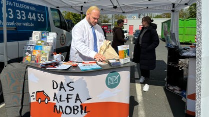 Oliver Meise steht am ALFA-Mobil Stand und sortiert Broschüren