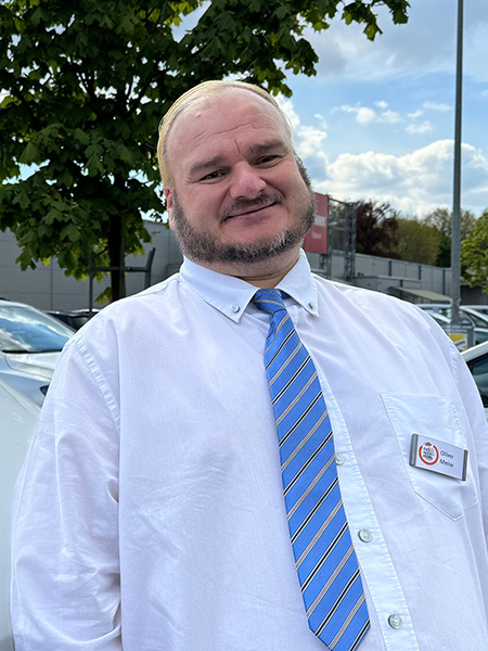 Ein Mann in Hemd und Krawatte steht neben einem Kleinbus