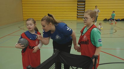 Handballtrainerin Ravn-Jörgensen erklärt zwei Kindern etwas auf dem Spielfeld