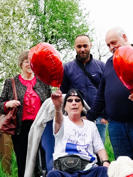 Martina sitzt im Rollstuhl. Um sie herum stehen Familie und Freunde mit Herzballons zum Geburtstag.