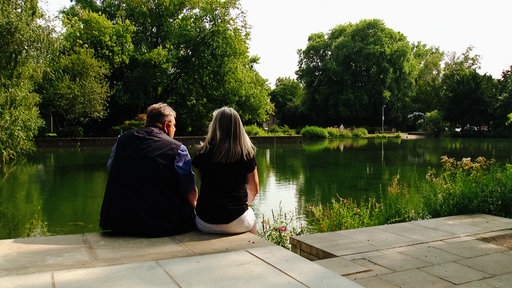 Eine Frau und ein Mann mittleren Alters, die an einem Teich sitzen und aufs Wasser blicken