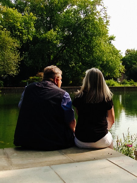 Eine Frau und ein Mann mittleren Alters, die an einem Teich sitzen und aufs Wasser blicken