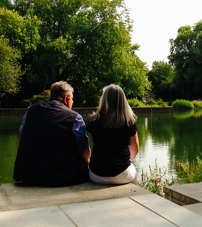 Eine Frau und ein Mann mittleren Alters, die an einem Teich sitzen und aufs Wasser blicken