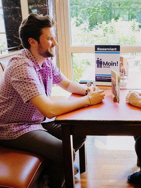 Ein Student und eine Seniorin sitzen sich in einem Café gegenüber und unterhalten sich.