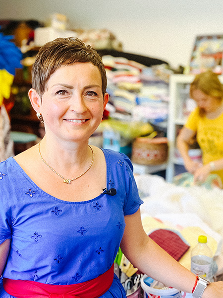 Natalya Franz steht an einem großen Nähtisch und lächelt in die Kamera.