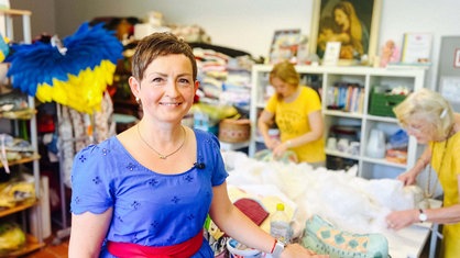 Natalya Franz steht an einem großen Nähtisch und lächelt in die Kamera.