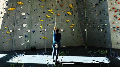 Eine Frau steht mit dem Rücken zur Kamera vor einer großen Kletterwand.