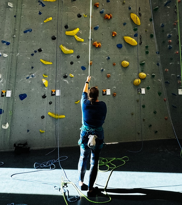 Eine Frau steht mit dem Rücken zur Kamera vor einer großen Kletterwand.