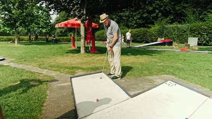 Friedhelm Niemann steht an einer Minigolfbahn und hält einen Schläger in der Hand