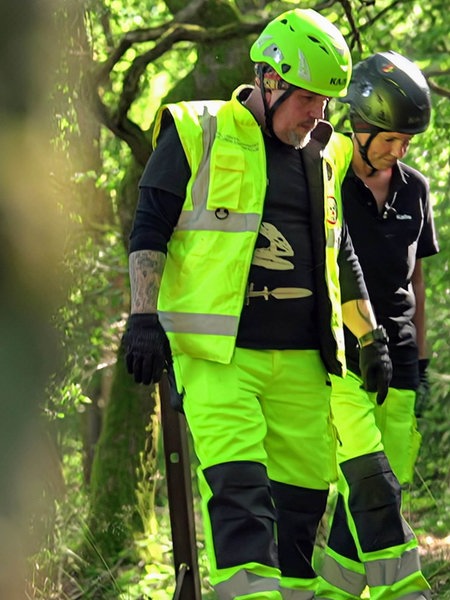 Zwei Menschen in gelber Warnkleidung in einem Wald.