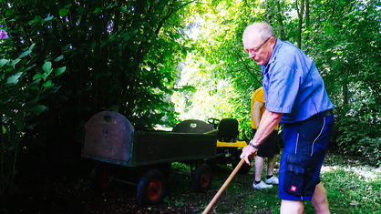 Robert Klein arbeitet mit einer Harke im Klostergarten: Im Hintergrund ist ein Bollerwagen mit einem kleinen Gartentraktor.