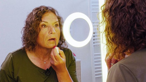 Nora Dahmer schaut in einen Spiegel mit Ringlicht, während sie sich Lipgloss aufträgt