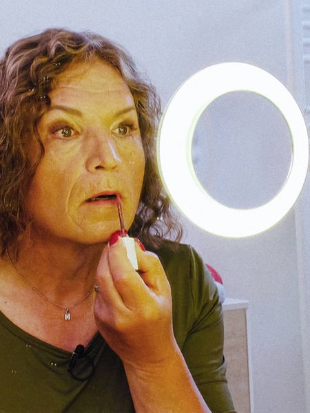 Nora Dahmer schaut in einen Spiegel mit Ringlicht, während sie sich Lipgloss aufträgt