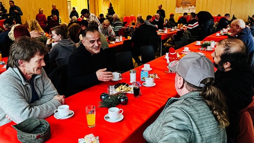 Erkan Nuran sitzt mit drei seiner Freunden am Tisch. Der Tisch befindet sich in einem gut gefüllten Saal.