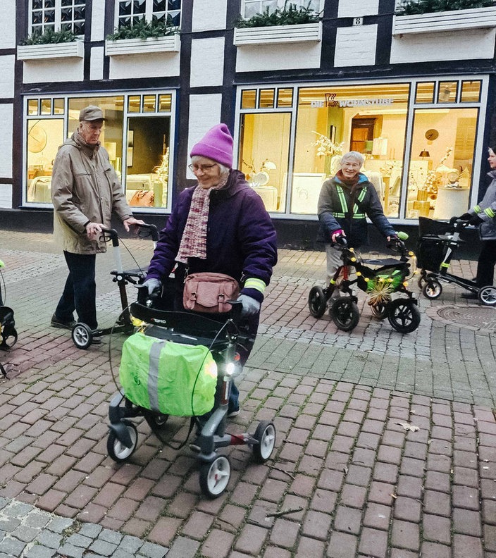 Die Innenstadt einer Kleinstadt. Mehrere Senioren mit Rollatoren gehen im Kreis