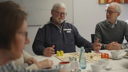 Schlaganfallhelfer Heinz Benking sitzt vor einem Mensch-ärgere-dich-nicht-Spiel, neben ihm andere Gruppenmitglieder