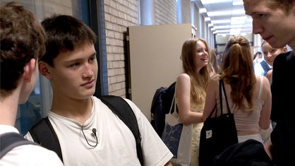 Drei Jugendliche stehen in einem Schulgang und unterhalten sich 
