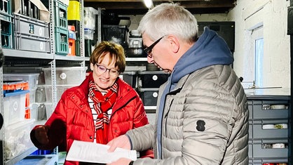 Ein Mann steht neben einer Frau in einem Geschirrlager. Beide blicken auf eine Liste in den Händen des Mannes.