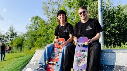 Fabio Navaro und Michael Franke sitzen auf einer Skateboardrampe, in der Hand halten sie ihre Skateboards