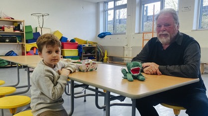 Der sechsjährige Loukas und Rentner Hartwig Kazcmarek sitzen an einem Tisch in der Schule und lernen gemeinsam Deutsch