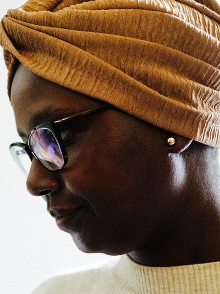 Eine Schwarze Frau mit Brille und orangenem traditionellen Turban auf dem Kopf