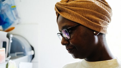 Eine Schwarze Frau mit Brille und orangenem traditionellen Turban auf dem Kopf