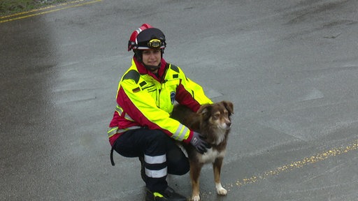 Eine Frau in rot-gelber Rettungskleidung hockt neben ihrem Hund mit braun-weißem Fell