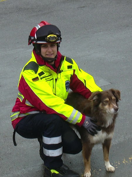 Eine Frau in rot-gelber Rettungskleidung hockt neben ihrem Hund mit braun-weißem Fell