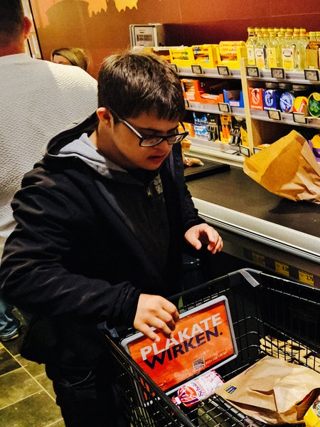 Ein Mann und eine Frau stehen in einem Supermarkt mit einem Einkaufswagen an einer Kasse.