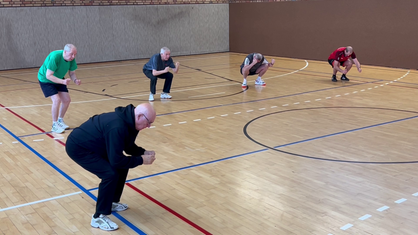 Senioren stehen in einer Sporthalle und machen Übungen