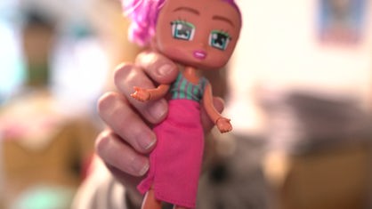 Eine Puppe mit pinken Haaren wird in die Kamera gehalten
