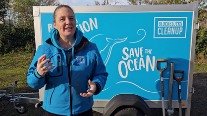 Eine Frau steht vor einem blauen Anhänger mit der Aufschrift "Save the Ocean".