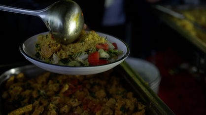 Eine silberne Kelle füllt marokkanisches Essen auf einen weißen Teller