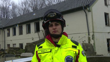 Frau in gelb-roter Rettungsuniform und mit Helm auf dem Kopf schaut in Kamera