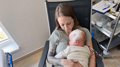Julia Korbach hat ihre Tochter als Baby auf dem Arm, am Kopf des Kindes kleben viele Pflaster 
