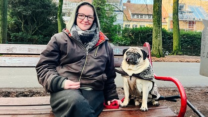 Eine Frau und ein Hund sitzen auf einer Bank und blicken in die Kamera