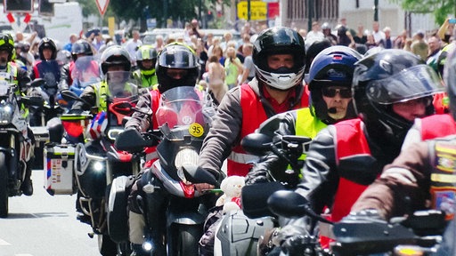 Motorradkorso in Düsseldorf. Links und rechts stehen Passanten und feuern die Fahrer an.