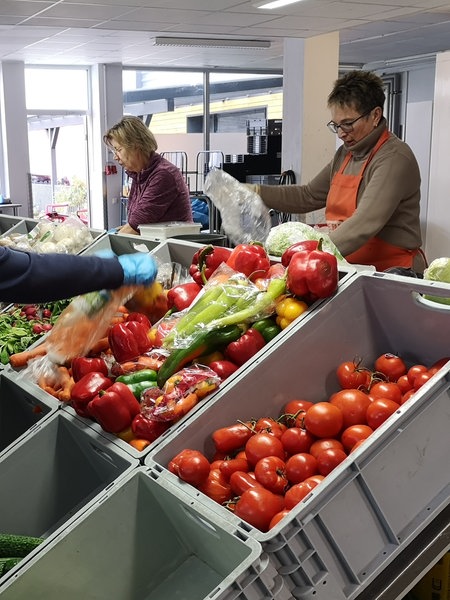 Frauen stehen vor Kisten mit Gemüse wie Tomaten, Gurken und Auberginen und sortieren dieses.