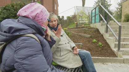 Zwei Frauen sitzen draußern auf einer Bank und unterhalten sich