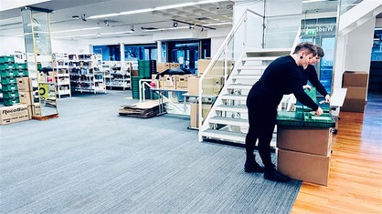 Eine Frau mit kurzen Haaren packt Umzugskartons in einer fast leeren Bibliothek