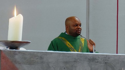 Ein Mann in einem grünen Priestergewand steht an einem Altar und spricht zur Gemeinde