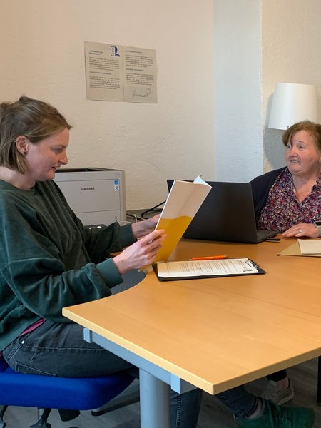 Die Mitarbeitenden Sara Hennes und Wilma Negroni sitzen an einem Schreibtisch und schauen sich Dokumente an.