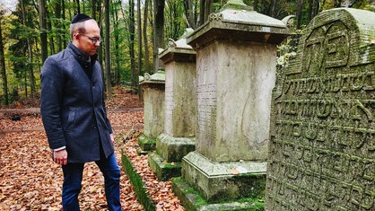 Sebastian Schröder im Wald. Er trägt eine Brille und eine Kippa. 