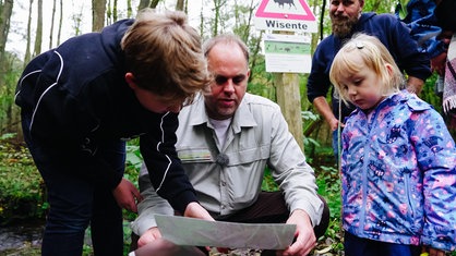 Förster Jan Preller erklärt Kindern mit Hilfe eines Fotos im Wald etwas über einen Biber