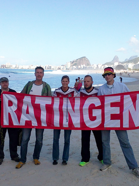 Zu sehen sind fünf Männer, die eine Ratingen-Fahne in der Hand halten. Sie stehen dabei an einem Strand.